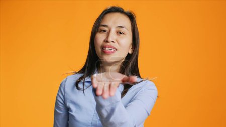 Photo for Joyful trendy filipino adult blowing air kisses in studio, posing with confidence over orange background. Positive woman showing romantic gesture, expressing flirt and sweet feelings. - Royalty Free Image