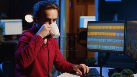 Foto de Fotógrafo que utiliza software en la computadora para realizar operaciones de edición, disfrutando de una taza de café mientras corrige imágenes. Editor de fotos usando PC para hacer ajustes a las fotografías en el estudio - Imagen libre de derechos