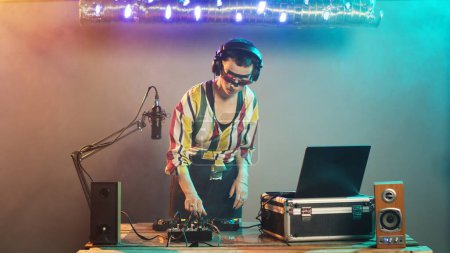Photo for DJ performer creating techno music at control buttons, wearing crazy makeup and mixing at audio stereo equipment. Artist playing disco sounds at turntables for nightclub party event. Tripod shot. - Royalty Free Image