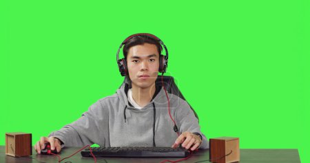 Foto de POV de hombre asiático juega videojuegos de PC en el escritorio, sentado sobre fondo de pantalla verde. Gamer divertirse con amigos en línea en el concurso de juegos, el uso de auriculares en la estación de trabajo. - Imagen libre de derechos