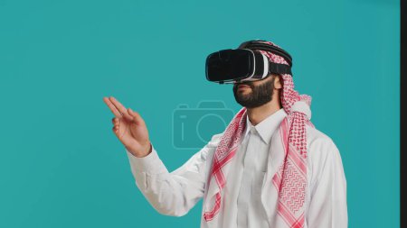 Photo for Middle eastern man using vr headset in studio, enjoying shoot with virtual reality technology on interactive glasses. Young person aving fun with 3d simulation, modern hobby and gadgets. - Royalty Free Image