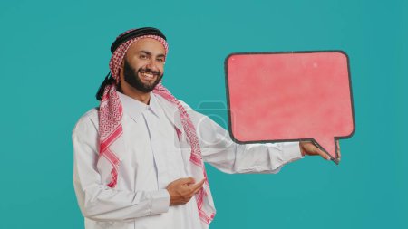 Photo for Muslim adult holds speech bubble on camera, creating advertisement for new web commercial. Young person working on marketing industry with empty cardboard icon, isolated billboard sign. - Royalty Free Image