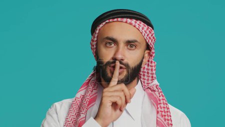 Photo for On camera, arabic person makes quiet signal with finger over lips, displaying silent mute gesture. In studio, private person does secretive confidentiality sign in an effort keep secret. - Royalty Free Image