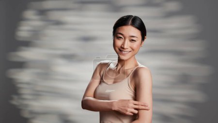 Téléchargez les photos : Asian woman promoting beauty products and cream in studio, creating skincare ad campaign for nourishing products. Flawless positive girl posing on camera to advertise tenderness. - en image libre de droit