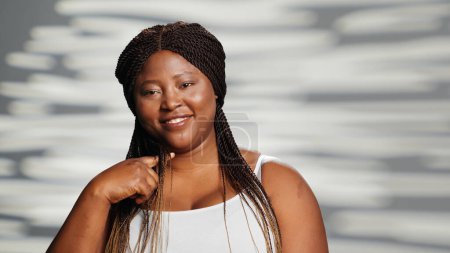 Téléchargez les photos : Positive girl with natural radiant skin posing in studio, creating skincare ad for body positivity. Young cheerful beauty model advertising self love acting confident and empowering. - en image libre de droit