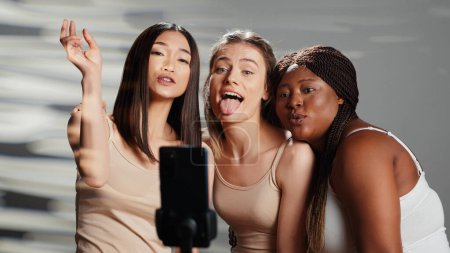 Foto de Grupo interracial de amigos tomando fotos en el teléfono inteligente para promover la autoaceptación y la positividad corporal. Las mujeres riendo y actuando divertido en las fotos, disfrutando de la campaña de anuncios de cuidado de la piel. - Imagen libre de derechos