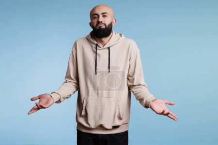 Photo for Arab man shrugging shoulders in doubt and confusion while looking a camera. Young person spreading arms in questioning gesture and making do not know signal studio portrait - Royalty Free Image