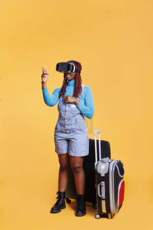 Téléchargez les photos : Modèle féminin portant des lunettes 3d vr en vacances, portant des sacs trolley et utilisant des lunettes de réalité virtuelle. Jeune femme s'amuser avec casque d'intelligence artificielle, voyager en vacances. - en image libre de droit