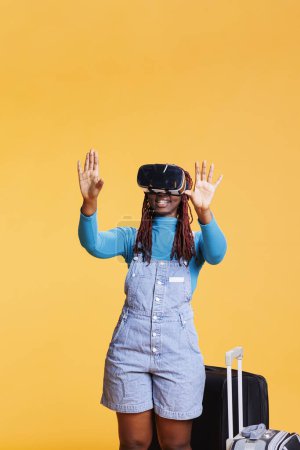 Foto de Mujer afroamericana con auriculares vr utilizando 3D visión interactiva que viaja en destino de vacaciones. Modelo femenino con gafas de realidad virtual en estudio, actividades de fin de semana. - Imagen libre de derechos