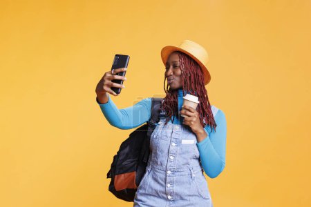 Téléchargez les photos : Fille afro-américaine prenant des photos sur la destination de vacances, se sentant heureux avec le café sur l'aventure urbaine en studio. Touriste féminine s'amuser avec des photos, escapade citadine funky. - en image libre de droit