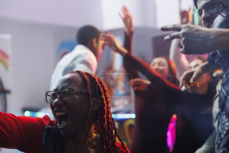 Foto de Mujer cantando en el micrófono en voz alta y gritando mientras festejaba con amigos en el club nocturno. Despreocupado afroamericano clubber gritando mientras se divierten y disfrutar de karaoke en el club - Imagen libre de derechos