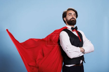 Téléchargez les photos : Puissant super-héros porte une cape rouge et se sent fort pour sauver les citoyens, posant sur fond bleu. Leader déterminé dans les vêtements formels agissant confiant, concept de dessin animé fantaisie. - en image libre de droit