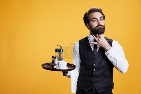 Photo for Stylish waiter posing with food tray against yellow background, preparing to serve coffee cup or meal. Confident elegant restaurant employee in front of camera, feeling determined. - Royalty Free Image