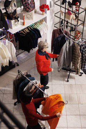 Photo for Multiple clients looking for xmas gifts and festive attire, people making preparations for christmas eve festivities and tradition. Retail store customers shopping for clothes during december season. - Royalty Free Image
