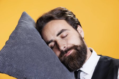 Photo for Tired butler using pillow to take nap in studio, feeling exhausted and sleepy after serving clients at five star restaurant. Professional worker resting head on camera, dealing with burnout. - Royalty Free Image