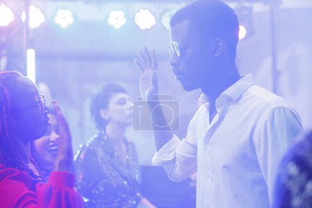 Photo for Man and woman dancing, making hands moves on club dancefloor illuminated with spotlights. Young african american dancers clubbing and enjoying nightlife in dark nightclub - Royalty Free Image
