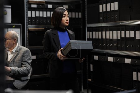 Téléchargez les photos : Comptable asiatique professionnel stockant des boîtes administratives de données analytiques dans le bureau de la salle d'armoire. Femme d'affaires professionnelle dans le stockage de fichiers lieu de travail bureaucratique - en image libre de droit