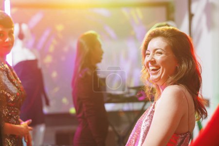 Foto de Sonriente mujer caucásica feliz riendo mientras está de fiesta en la discoteca en la pista de baile en el club nocturno con focos. Chica alegre bailando y divirtiéndose, disfrutando de ocio nocturno en el club - Imagen libre de derechos