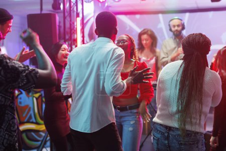 Téléchargez les photos : Amis dansant à la fête disco et clubbing tout en profitant de la vie nocturne loisirs. Diverses personnes faisant des mouvements au rythme de la musique électronique sur la piste de danse dans une boîte de nuit avec des projecteurs - en image libre de droit