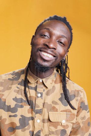 Photo for Attractive joyful man smiling at camera, having fun while posing over yellow background. Relaxed african american person with positive facial expression, enjoying free time during studio shot - Royalty Free Image