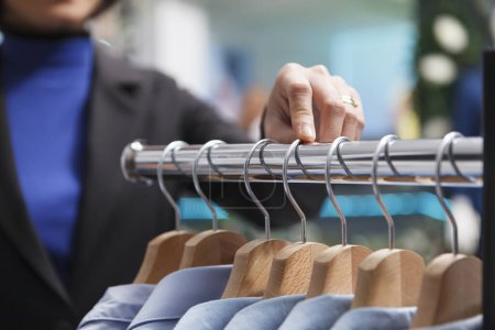 Photo for Clothing store assistant hand counting apparel on rack, checking and adjusting merchandise in stock closeup. Shopping center showroom employee arm managing garment inventory - Royalty Free Image