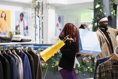 Foto de Mujer afroamericana feliz bailando con bolsas de compras después de hacer una compra exitosa en la tienda de ropa. Alegre shopaholic llevar paquetes de papel con ropa de moda en boutique - Imagen libre de derechos