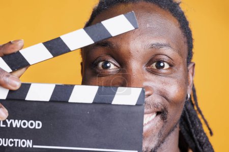 Photo for Portrait of man holding clapperboard to cut scenes in movie industry, posing on yellow background. African american man working in film making production and cinematography in studio. - Royalty Free Image