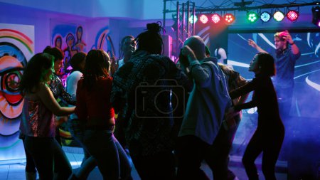 Foto de Diversas personas se divierten divirtiéndose en el club, bailando en la actuación de música en vivo con luces brillantes de colores. Hombres y mujeres jóvenes disfrutando de la fiesta disco, reunión social. Disparo de mano. - Imagen libre de derechos