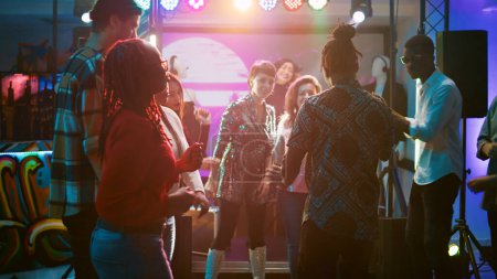 Photo for Men and women having fun at dance party with electronic music, showing modern robot moves on dance floor. Cheerful friends dancing at social gathering, clubbing event. Handheld shot. - Royalty Free Image