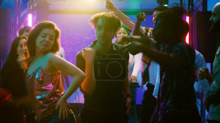 Téléchargez les photos : Divers amis sautant à la soirée dansante, s'amusant avec des projecteurs et de la musique électronique au club. Des hommes et des femmes talentueux exhibant des mouvements de danse cool pour une bataille de breakdance improvisée. Trépied. - en image libre de droit