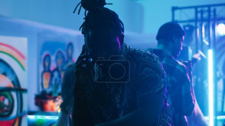 Photo for Young man talking on smartphone at club, trying to chat with someone on mobile phone call in discotheque. Modern adult attending funky disco party at nightclub, answering phone. - Royalty Free Image