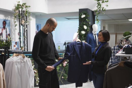 Photo for Shopping center boutique woman worker holding jacket on hanger, assisting arab customer in choosing outfit. Clothing store asian employee consulting client, helping with purchase - Royalty Free Image