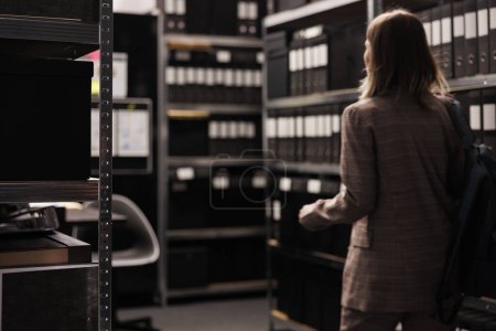 Photo for Selectiv focus of metallic storage full with administrative files, arhive room equipped with bureaucracy documents. Corporate employee working late at night searching for accountancy report - Royalty Free Image