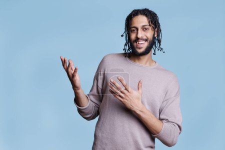 Photo for Carefree arab man gesticulating with arms while smiling and looking at camera. Young adult handsome person wearing casual clothes expressing joy und pointing upwards portrait - Royalty Free Image