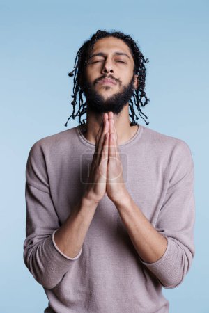 Photo for Arab man praying to god with folded hands and making wish with closed eyes. Young person with hopeful facial expression of peace and spirituality pleading for forgiveness concept - Royalty Free Image