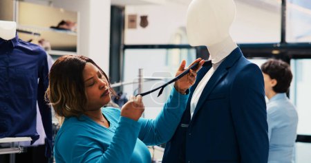 Téléchargez les photos : Acheteur afro-américain analysant en costume bleu, vérifiant le matériel de marchandises dans le magasin de vêtements. Achats de vêtements à la mode, en regardant la nouvelle collection de mode - en image libre de droit