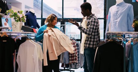 Photo for African american couple checking stylish merchandise, shopping for casual wear in modern boutique. Fashionable customers analyzing trendy outfit material in clothing store. Fashion concept - Royalty Free Image