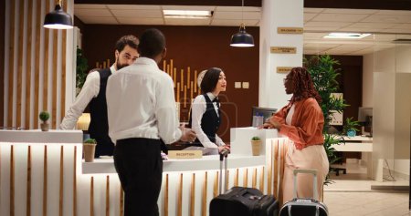 Photo for Friendly smiling concierge personnel assisting tourists with room registration. Cheerful front desk receptionists answering customer inquiries about hotel amenities during guests check in process - Royalty Free Image