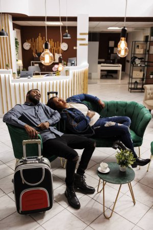 Téléchargez les photos : Couple fatigué dormant dans le hall de l'hôtel après un long vol international, souffrant de fatigue de voyage et de décalage horaire. Touristes épuisés faisant la sieste allongés sur le canapé en attendant l'enregistrement à la station - en image libre de droit