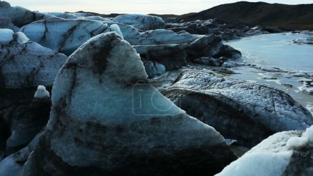 Téléchargez les photos : Drone shot of vatnajokull glacier mass, beautiful blue ice blocks with crevasses and icebergs near snowy mountains. Rochers glacés massifs avec givre flottant sur le lac. Mouvement lent. - en image libre de droit