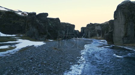 Foto de Islandés fjadrargljufur cañón drone disparo con hermosos paisajes fluviales y nórdicos, montañas nevadas y colinas. Paisaje ártico junto a la carretera con agua que fluye entre rocas y acantilados. Movimiento lento. - Imagen libre de derechos