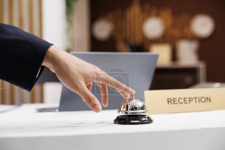 Photo for Business traveller rings service bell at reception counter, calling for employees assistance after arriving at luxury hotel. Businessman using bell at front desk, ready for check in. Close up. - Royalty Free Image