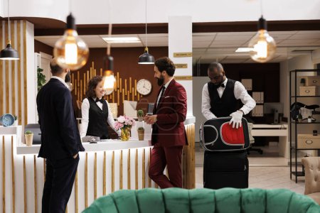 Photo for Colleagues greeted by receptionist at front desk, partners in suits arriving at luxury hotel to attend executive business meeting, travelling for work. Men on journey, conference participation. - Royalty Free Image