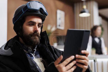 Photo for Detailed view of winter traveler holding tablet in hotel lobby, surfing the net for their snowy adventure. Close-up of man grasping a smart device for research on winter holiday activity. - Royalty Free Image