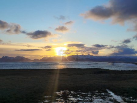 Téléchargez les photos : Paysage lacustre arctique au coucher du soleil avec ciel doré et montagnes enneigées, nature sauvage scandinave créant des paysages fantastiques. Massive front de mer de l'océan autour de la campagne icelandique. - en image libre de droit