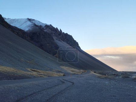 Foto de Paisaje rocoso islandés en carretera, camino solitario en clima invernal nórdico con desierto vacío. Camino largo congelado con cadena montañosa masiva y acantilados en iceland, ruta escénica. - Imagen libre de derechos
