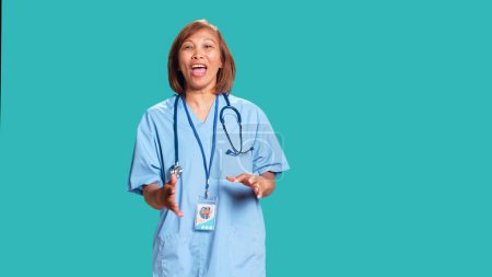 Photo for Angry healthcare specialist yelling furiously and aggressively gesticulating while at work. Outraged asian nurse, isolated over blue studio background shouting threateningly - Royalty Free Image