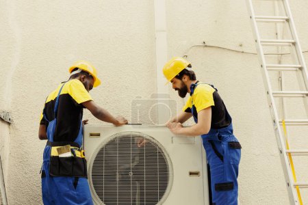 Photo for Expert master technician and apprentice serviceman dismantling old busted external air conditioner to replace it with new performant hvac system after draining refrigerant and replacing ductwork - Royalty Free Image