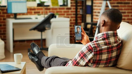 Photo for Man checking up on abroad living friend during video conference meeting over the internet. African american mates enjoying time together in online video call session while at home - Royalty Free Image