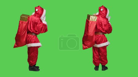 Photo for Sweet saint nick sends air kisses to spread romance and chrsitmas holiday spirit, acting flirty and cute over full body greenscreen backdrop. Person dressed as santa claus character in costume. - Royalty Free Image